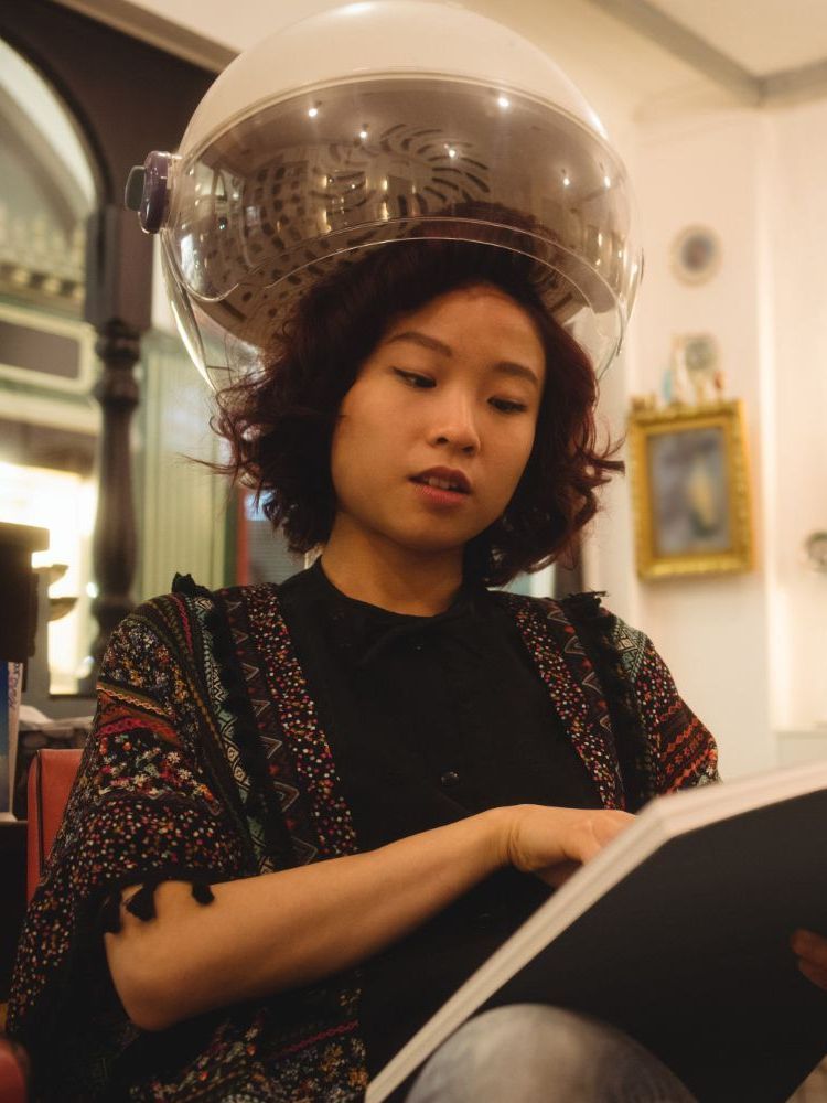 A woman with a hair dryer on her head is reading a book